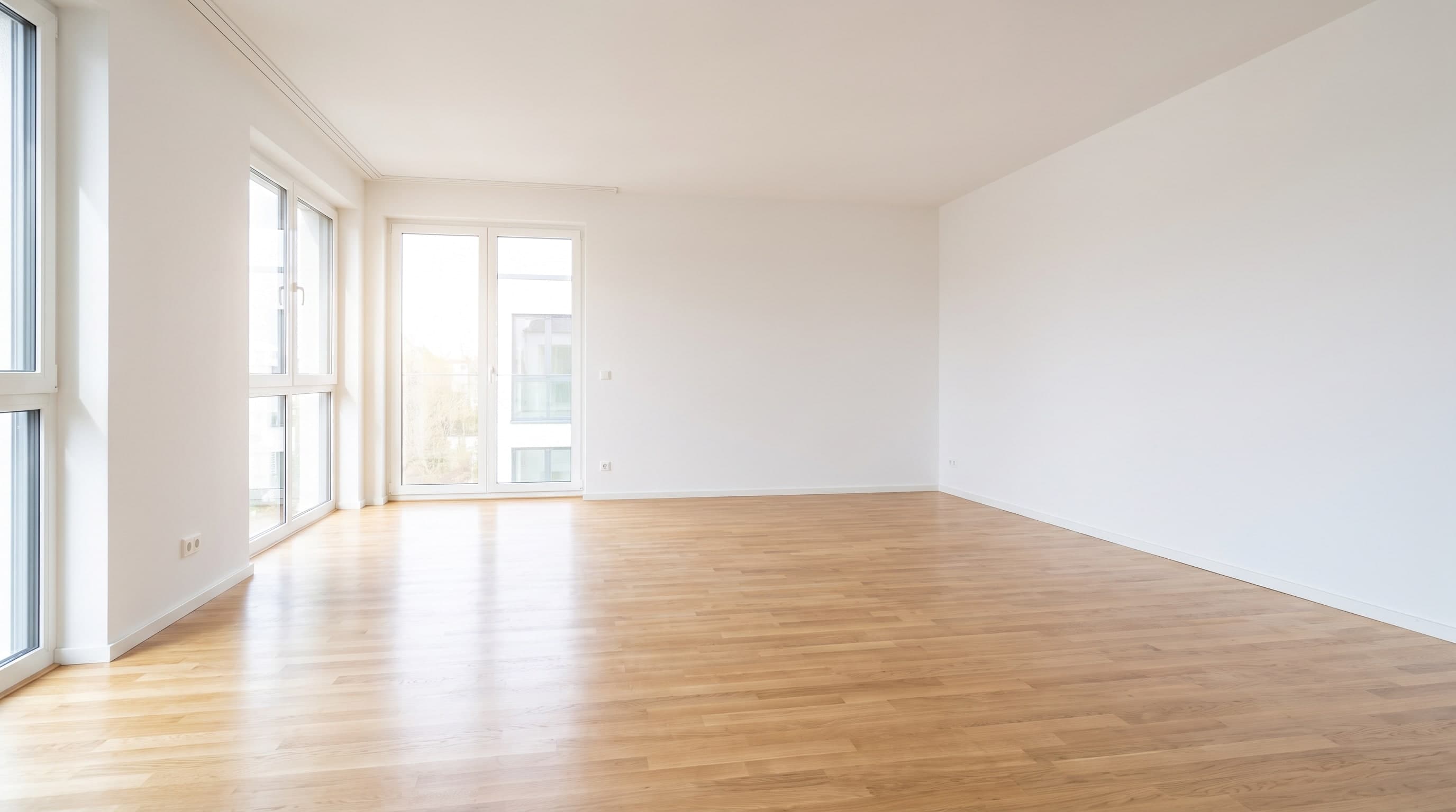 Leerer, heller Raum mit Parkettboden und großen Fenstern